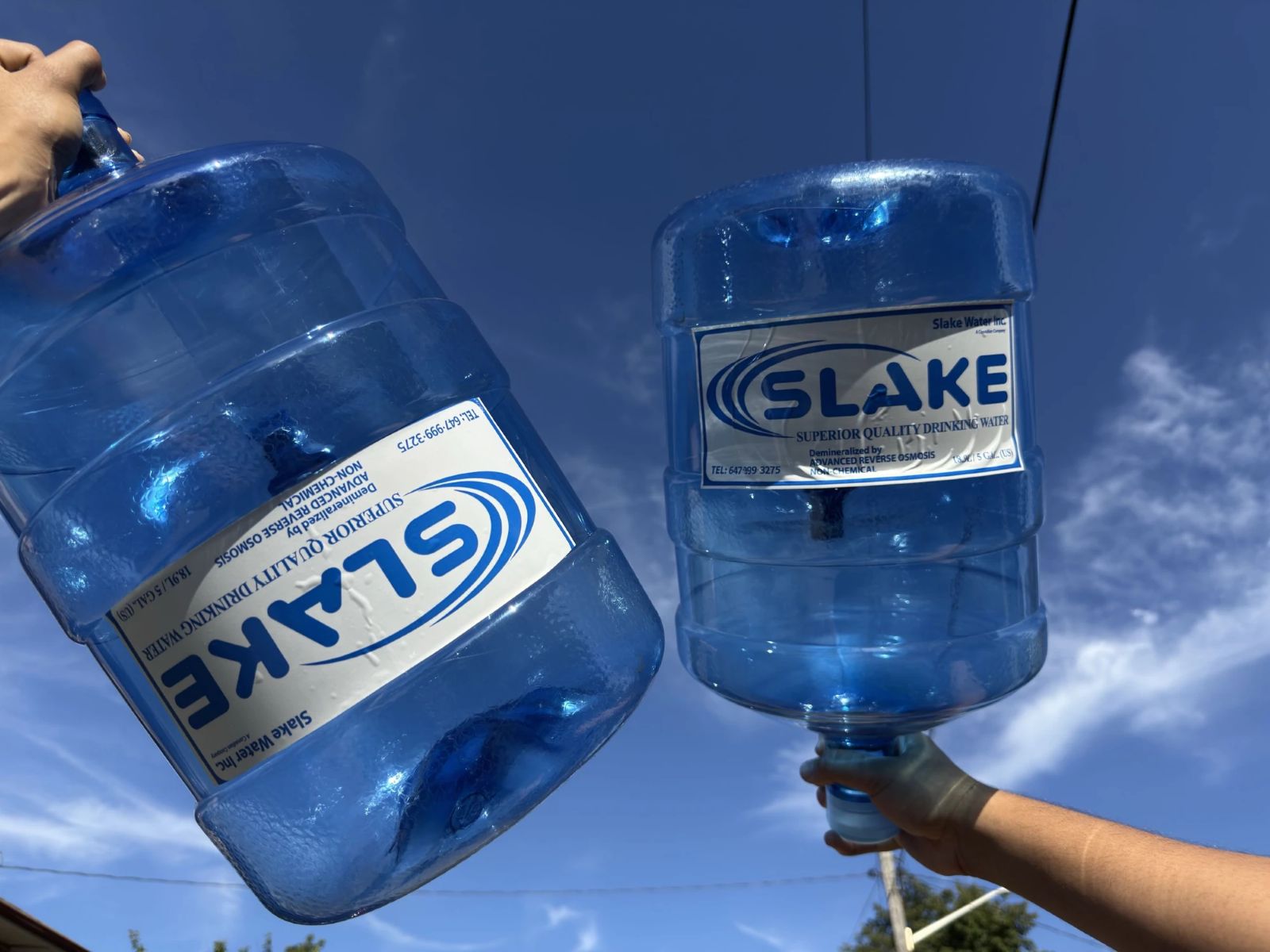 Two Slake Water 5-gallon bottles held up against a blue sky